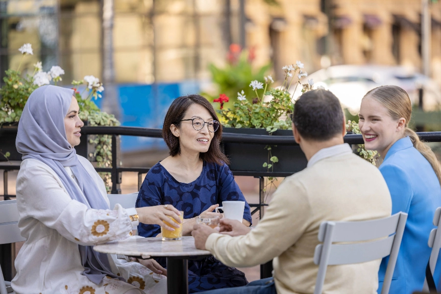 Four international people chatting in a street cafe  - Marjaana Malkamäki / Keksi