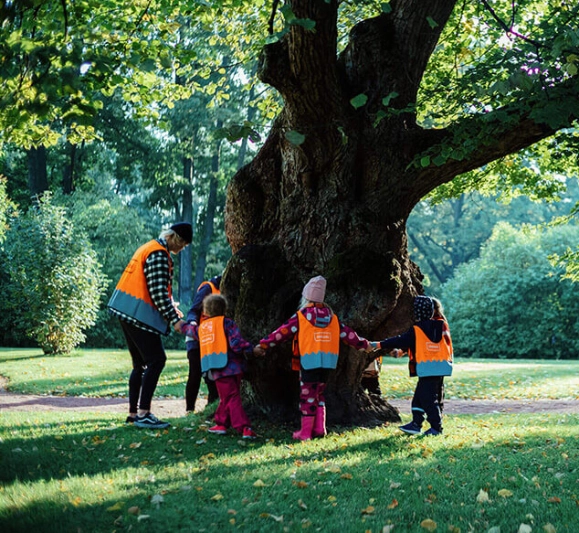 Children in bright orange vests circling a tree. - Jussi Hellsten / Helsinki Partners