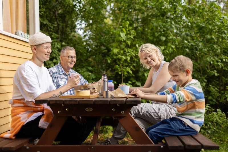Four people sitting at a garden outside cottage - Marjaana Malkamäki / Keksi