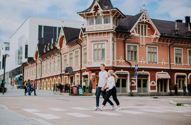 A couple crosses the street in front of a pink Victorian building. - Julia Kivelä / Finnish Lakeland /Jyväskylä Region