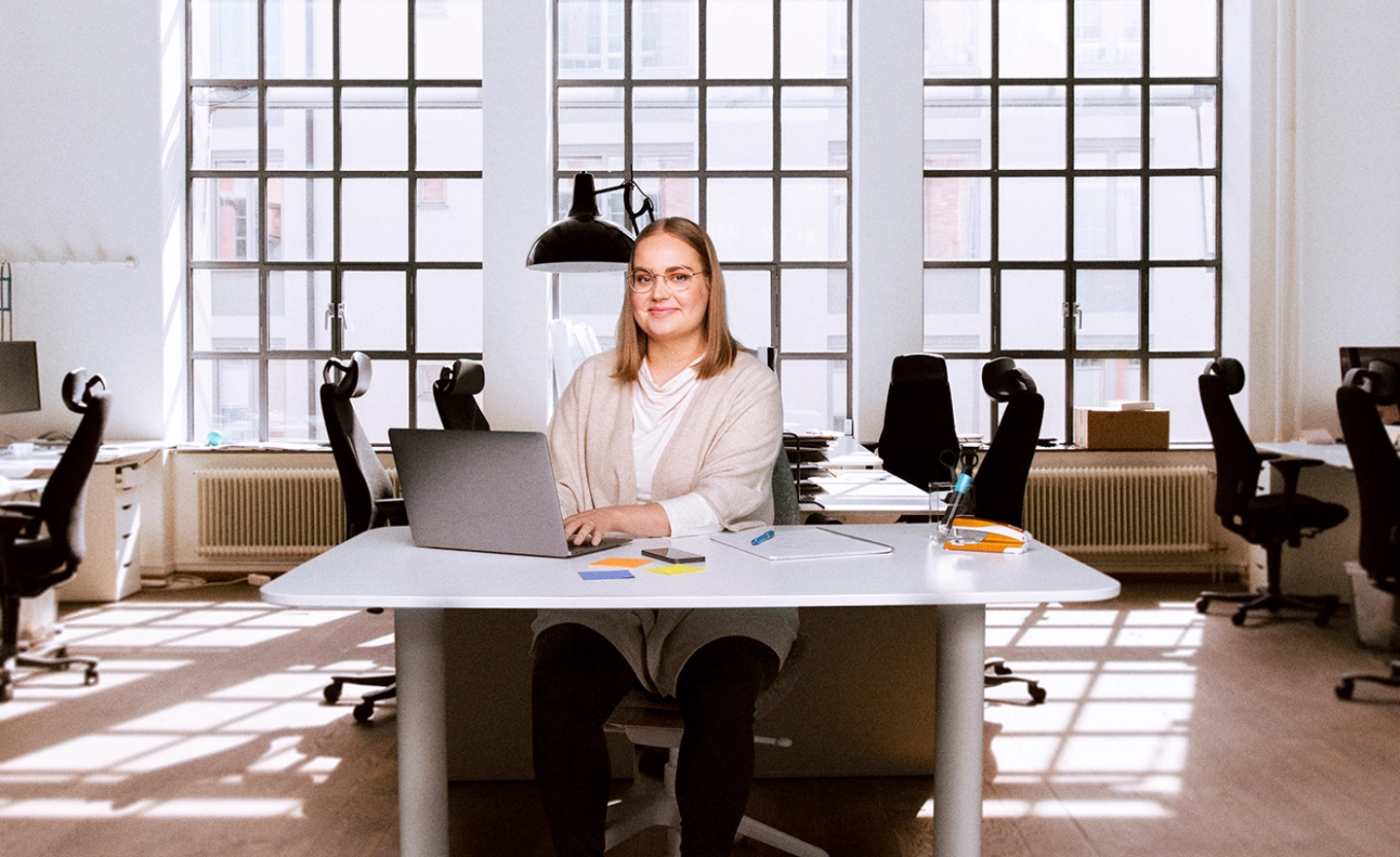 Työnantajaneuvonnan asiakaspalvelija istuu työpöydän ääressä keskellä start-up-toimistoa - Work in Finland International Recruitment Advice Service for Employers